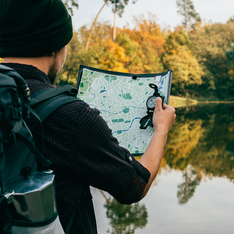 over the shoulder shot of a hiker holding a compass and a map