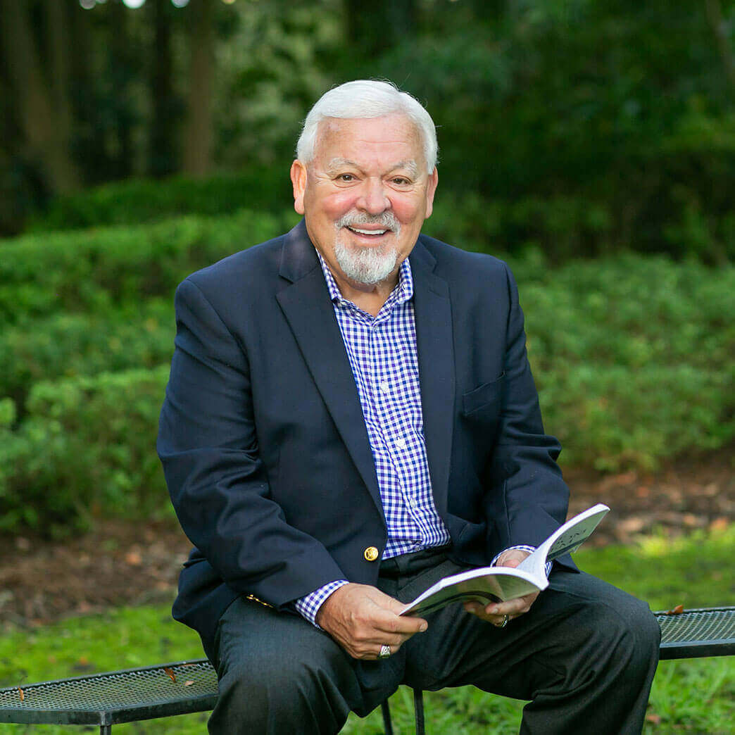 Charlie smiling and holding a book, sitting on a bench in front of green shrubbery